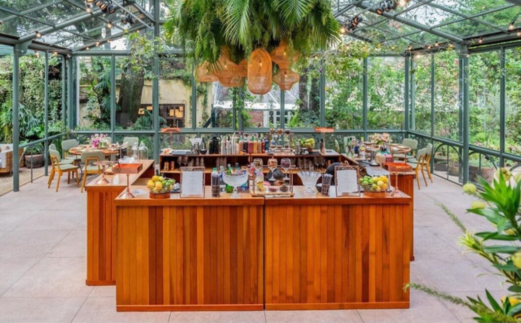 Bar de madeira montado em estufa de vidro com jardim ao redor